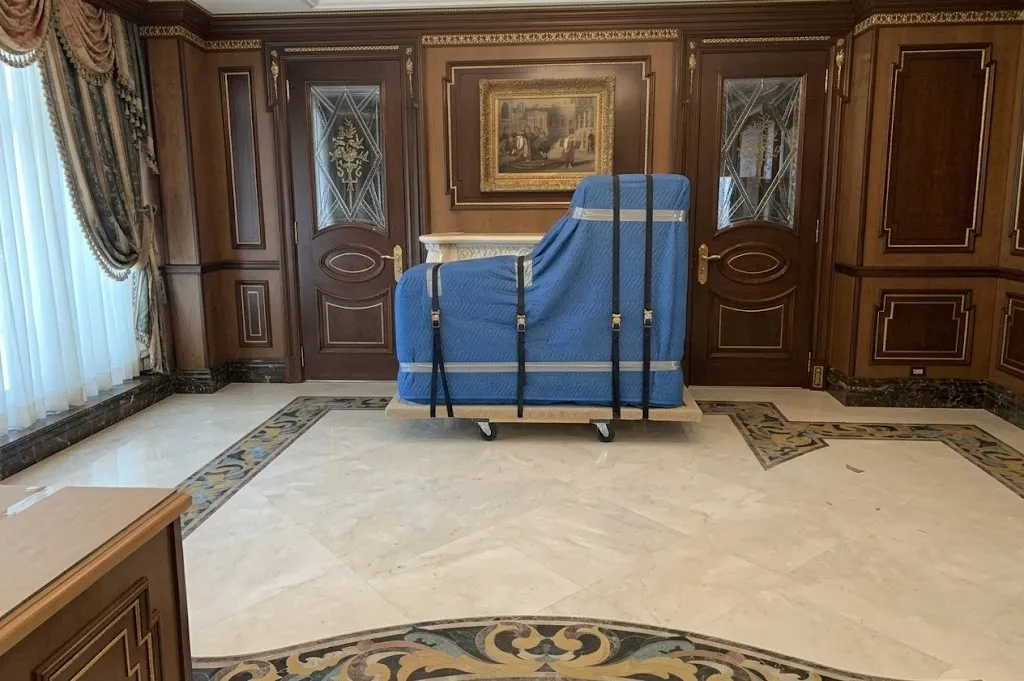 Grand piano encased in protective blue quilted blankets and secured with straps