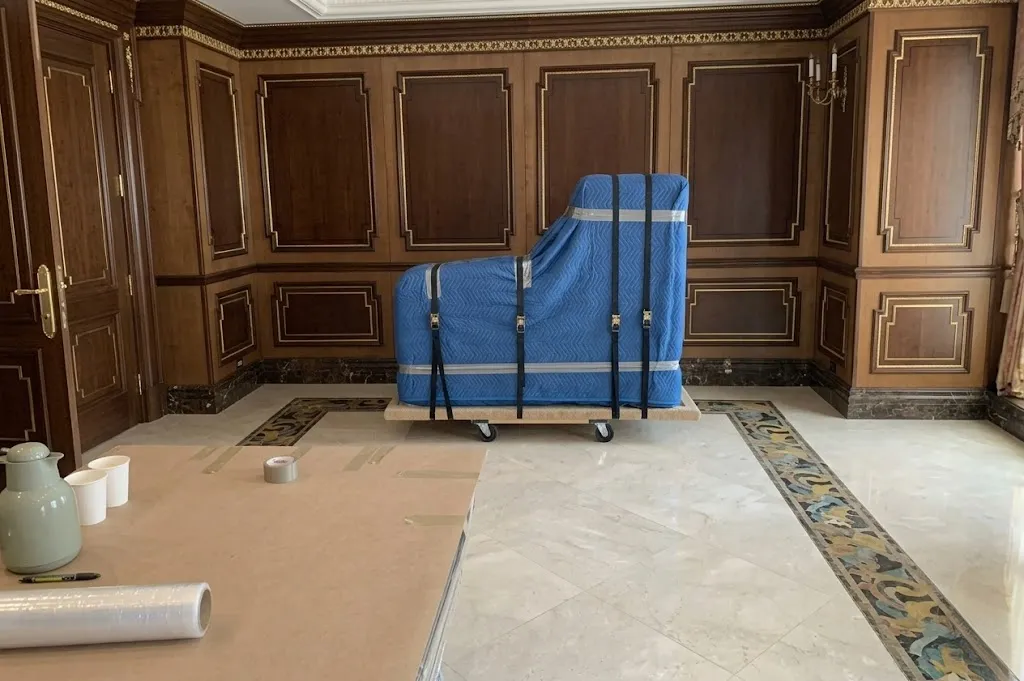 Grand piano encased in protective blue blankets secured on a dolly